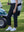 Lower body view of model carrying golf bag in Women's 7/8 ankle golf track pants, black