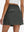 Back lower body shot of model wearing dark grey women's stretch a-line golf skort with 7 pockets