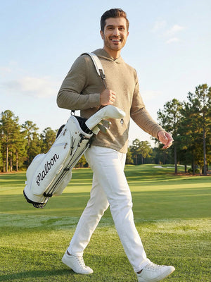 Model holding a golf bag on a golf course, wearing light brown heather texture solid hoodies pullover in full-body view.