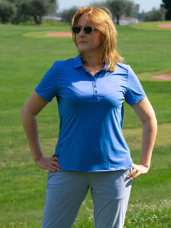 A model wearing the Women's Performance Solid Polo stands on the grass